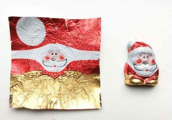 A foil-wrapped chocolate Santa next to a flattened wrapper printed with the same Santa