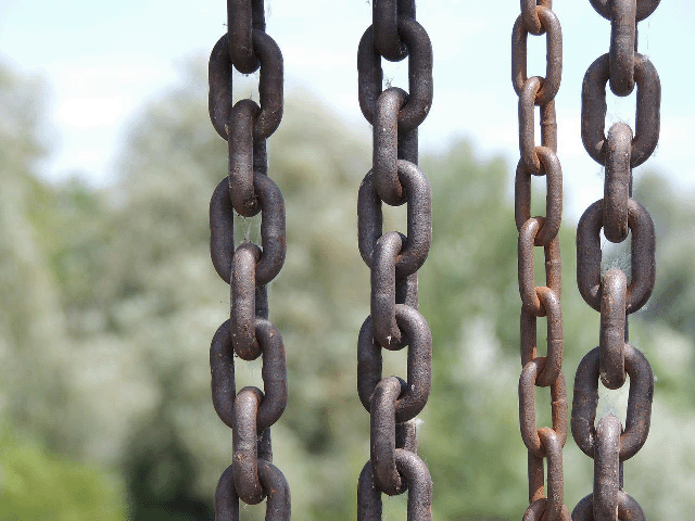 A series of partially rusted chains hanging vertically with a blurry background.